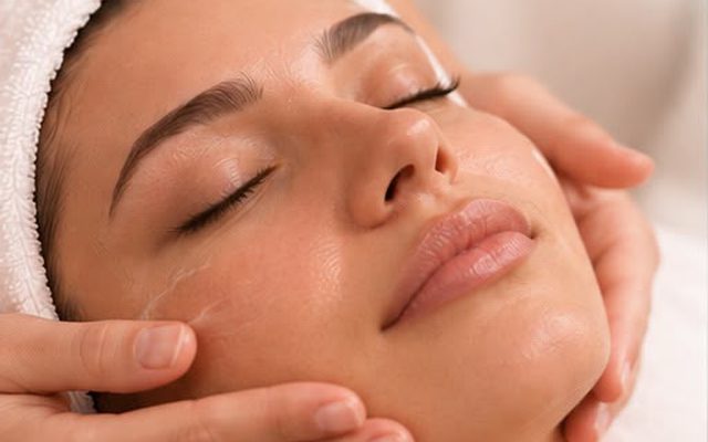 Ilustração: massagem facial em uma cliente de olhos fechados, com toalha no cabelo.